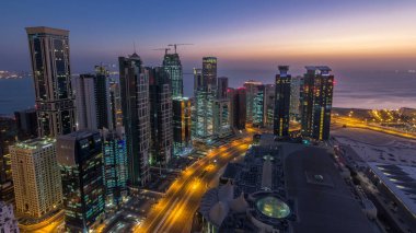 Batı Körfezi bölgesinin ufuk çizgisi Doha 'da gece gündüz geçiş zamanı, Katar. Aydınlatılmış modern gökdelenler. Sabah güneş doğmadan önce çatıdan gökyüzü manzarası.