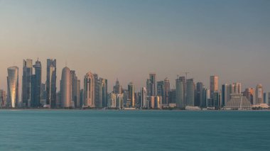 Katar 'ın Doha şehrinin ufuk çizgisi sabahın erken saatlerinde güneşin zengin ılık renkleri cam gökdelenlerden yansıyor..
