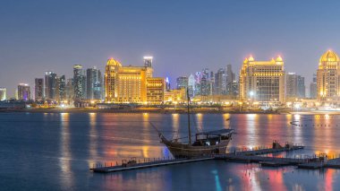Katara Sahili 'nden gece gündüz geçiş zamanlarını Doha, Katar' da, Batı Körfezi ve şehir merkezine doğru izleyin. Aydınlatılmış gökdelenler. Öndeki eski gemi
