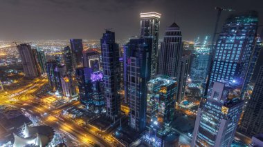 Katar 'ın Doha Zaman Çizelgesi' nde Batı Körfezi bölgesinin ufuk çizgisi. Aydınlatılmış modern gökdelenler geceleri çatıdan gökyüzü manzarası. Yolda trafik vardı.
