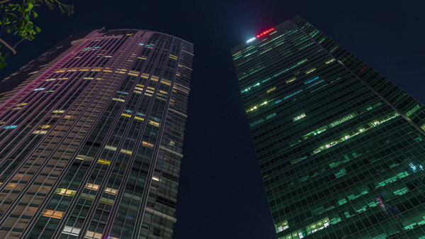 Looking up perspective of modern business skyscrapers glass and starry sky view landscape of commercial building in central city timelapse. Towers with glowing windows in Singapore.