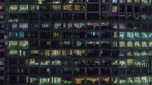 Gece vakti büyük pencereleri olan modern ofis binası. Yakın görüş, parlayan pencereler ve Singapur 'da yaşayan bazı insanlar.