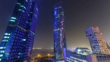 Katar 'ın Doha Zaman Çizelgesi' nde Batı Körfezi bölgesinin ufuk çizgisi. Aydınlatılmış modern gökdelenler geceleri çatıdan gökyüzü manzarası. Arka plandaki körfez ve yoldaki trafik