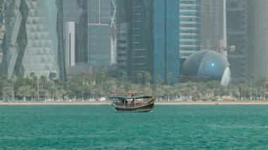 Güneşli bir günde arka planda şehrin modern silueti olan Doha Timelapse, Katar 'da limana giden bir dhow.