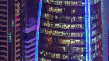 İçerideki cam ve çelik ofis aydınlatması ve çalışan insanların çok katlı binasının zaman çizelgesi. Gökdelenlerin gece aydınlanması. Doha, Katar