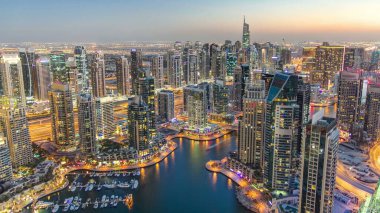 Dubai Marina 'da yatlar ve gece gündüz hava geçiş panoramik zaman dilimi. Mavi gökyüzü ile açık bir akşamda parlak ışıklar ve en yüksek gökdelenler. Gün batımından sonra yukarıdan görünüm