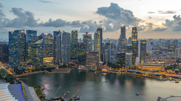 Aerial view of Singapore business district skyscrapers at evening with water reflections day to night timelapse. Panorama of illuminated towers with blinking lights in windows