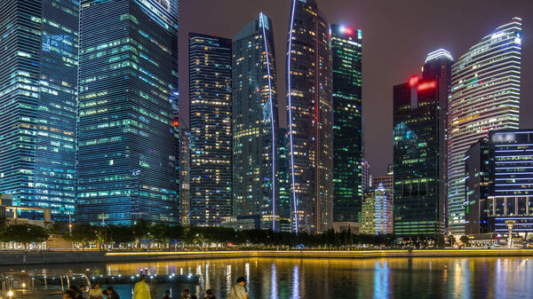 Singapore business district skyscrapers in the night time with water reflections timelapse hyperlapse. Illuminated towers with blinking lights in windows