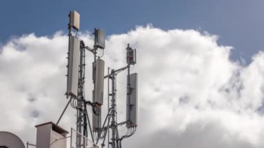 Telekomünikasyon kulesi zaman ayarlı beyaz bulutlar ve mavi gökyüzü arka planda. Çatıda kablosuz iletişim anteni vericisi var. 3G, 4G ve 5G Hücre Sitesi