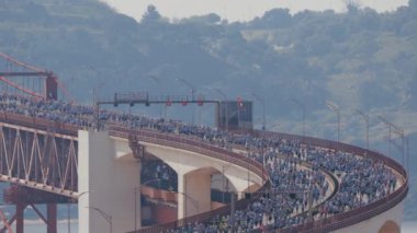Lizbon 'da koşmak 25 Nisan köprüsünü yukarıdan Tagus nehri hava manzarası üzerinden geçmek demek. Büyük bir kalabalık baştan sona köprüden aşağı ilerliyor. Yolun kıvrımlı kısmı. Isı dalgaları
