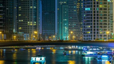 Gece vakti Dubai Marina kanalında trafik olan gezinti ve köprü, BAE. Palmiyeler, tekneler ve aydınlık kulelerle köprüden görüntü. Yapay kanallı bölge