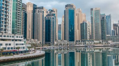 Dubai Marina 'daki köprüden sabah görüntüsü su ve gezinti saatlerine yansıyan modern kuleler Birleşik Arap Emirlikleri. Yapay kanalı olan bir bölge. Mavi bulutlu gökyüzü