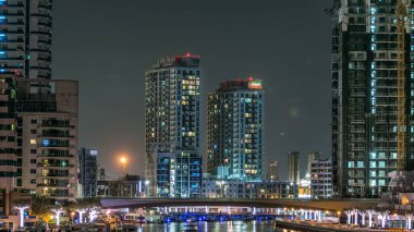 Gece Dubai Marina 'da gezinti zamanı, BAE. Palmiyeler, yüzen tekneler ve konut kuleleri ile rıhtım manzarası. Dubai 'de yapay kanallı bir bölge.