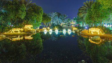 Kaplanlar ve ağaçlarla dolu bir göl. Dubai Işıltılı Bahçesi 'nde aydınlanmış ağaçlar ve heykeller. Çevre dostu mimarinin yer aldığı, çeşitli yapılar yaratan bir sanat devleti.