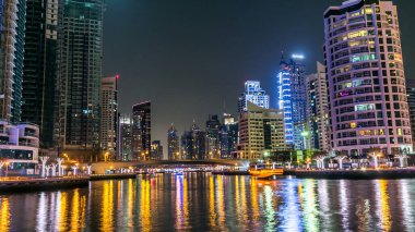 Dubai Marina gezinti güvertesinde yatlar ve modern kuleler Dubai 'deki deniz kıyısından yansıyan su, Birleşik Arap Emirlikleri. Köprü ve gökdelenler