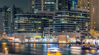 Gece Dubai Marina 'da gezinti zamanı, BAE. Palmiyeler, yüzen tekneler ve modern kulelerle köprüden manzara. Yapay kanallı bölge