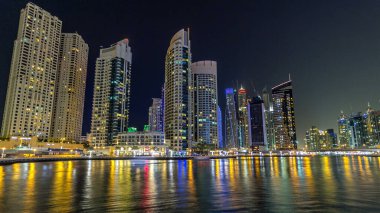 Dubai Marina gezinti güvertesinde yatlar ve modern kuleler Dubai 'deki deniz kıyısından yansıyan su, Birleşik Arap Emirlikleri' nin gece hiperhızlandırması. Yapay kanalla aydınlatılmış bölge