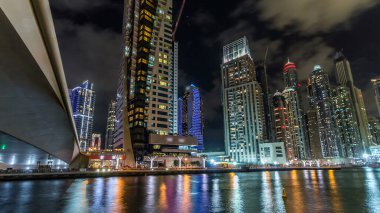 Dubai Marina güvertesi, deniz kenarındaki Birleşik Arap Emirlikleri gecesinden kalma yatlar ve modern kulelerle doludur. Çevresinde yapay kanallar ve aydınlık gökdelenler olan bir bölge.