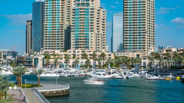 Dubai Marina gezinti güvertesi, palmiyeler, yüzen yatları olan modern kuleler ve köprü zamanından kalma botlar, Birleşik Arap Emirlikleri. Yapay kanal ve gökdelenler