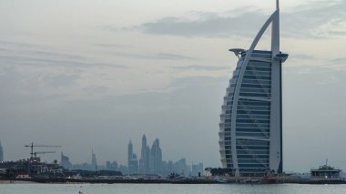 Dubai silueti, Burj Al-Arap oteli ile gündüz gece geçiş zamanı. Uçurtma kumsalının manzarası. Dubai marina kuleleri arka planda. Jumeirah plajının önünde yapay bir adaya inşa edilmiş bir otel..