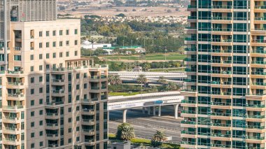 Golf sahası ve Dubai silueti gündüz vakti Şeyh zayed yolunda trafik varken. Golf sahasının yeşil çimenleri arka planda şehrin gökdelenleri gün batımında. Yan taraftaki modern kuleler