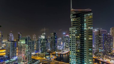 Dubai Marina gezinti güvertesi ve kanalı, Dubai, BAE 'de yüzen yat ve tekneleri olan hava manzaralı. Yanıp sönen ışıkları ve yol trafiği olan aydınlık modern kuleler