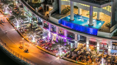 Dubai Marina 'nın gece gezintisi sırasında Dubai, BAE' de yüzen yatları ve tekneleri olan restoran ve kanallarla hava manzaralı. Yanıp sönen ışıkları ve yürüme alanı olan aydınlık modern kuleler