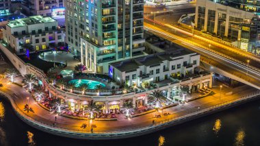 Dubai Marina yürüyüş alanının gece hava manzarası. Dubai, BAE 'de yüzen yatları ve tekneleri olan restoranlar ve kanallar var. Köprüde ışıkları ve trafiği olan modern kuleler.