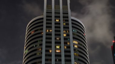 Geceleri iş yerlerindeki modern binaların zaman çizelgelerine bak. Parlak pencereli cam cepheli gökdelenler. Ekonomi ve finans kavramı. Dubai, BAE