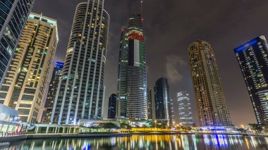 Rıhtımdaki ışıklandırılmış gökdelenlerin gece görüş açısını hızlandırın. Dubai, BAE 'deki Jumeirah Gölü Kuleleri' ndeki konut binaları. Rıhtımdan görüntüle