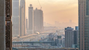 Akşam saatlerinde Dubai Kuleleri 'nin aşağısında. Gün batımında Şeyh Zayed 'in gökdelenli hava manzarası. Yol kavşağında ve metro hattında trafik vardı. Güzel turuncu gökyüzü