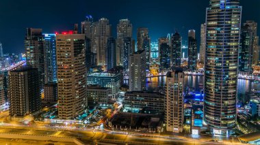 Dubai Marina gezinti güvertesi ve kanalı, Dubai, BAE 'de yüzen yat ve teknelerle dolu. Yanıp sönen ışıkları ve yol trafiği olan aydınlık modern kuleler.