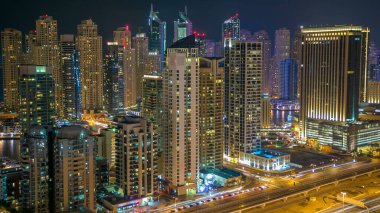 Dubai Marina gezinti güvertesi ve kanalı, Dubai, BAE 'de yüzen yat ve teknelerle dolu. Yanıp sönen ışıkları ve yol trafiği olan aydınlık modern kuleler.
