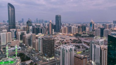Abu Dabi gökdeleninin modern şehir mimarisi günden geceye geçiş havası, BAE. Aydınlatılmış gökdelenler ve yol trafiği. Abu Dabi Birleşik Arap Emirlikleri 'nde en kalabalık ikinci şehirdir.