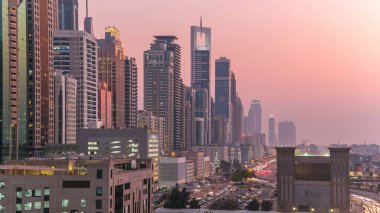 Dubai Kuleleri 'nin şehir merkezinden gece gündüz geçiş zamanı. Gün batımından sonra Şeyh Zayed 'in gökdelenli hava manzarası. Yolda ve otoparkta trafik vardı.