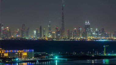 Gece vakti Dubai şehir merkezinin silüeti. Çölde inşa edilmiş modern gökdelenlerin manzarası. Palm Jumeirah 'dan suya yansıyan üst hava görüntüsü