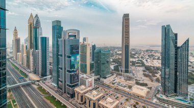 Dubai downtown skyline timelapse at sunset with financial center skyscrapers and Sheikh Zayed road traffic. Top aerial view from tower rooftop. Clouds on the sky. Dubai, United Arab Emirates