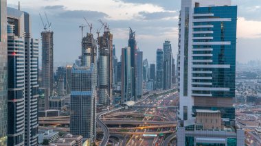 Dubai şehir mimarisi günden geceye geçiş zamanı. Şeyh Zayed yolu üzerindeki gökdelenler aydınlanmış ve kavşakta trafik var. Güzel bulutlu gökyüzü