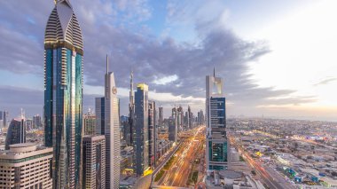 Dubai şehir mimarisi günden geceye geçiş zamanı. Şeyh Zayed yolu üzerindeki aydınlık gökdelenler ve trafik manzaralı üst hava manzarası. Güzel bulutlu gökyüzü