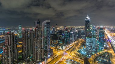 Dubai iş hangarı kuleleri gece vakti aydınlatılıyor. Kavşakta trafik vardı. Bazı gökdelenlerin çatısı ve inşaat halindeki yeni kulelerin havadan görüntüsü.