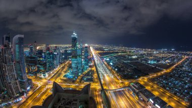 Dubai iş hangarı kuleleri gece aydınlandı. Dubai su kanalı, köprüler ve Şeyh Zayed yolu trafiği. Bazı gökdelenlerin çatı manzarası ve inşaat halindeki yeni kuleler. Bulutlu gökyüzü
