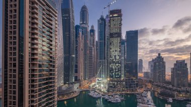 Dubai Marina 'da gün doğumundan önce Dubai, BAE' de yatlarla birlikte gece gündüz en yüksek modern gökdelenlerin hava manzarası. Sabahın erken saatlerinde aydınlık kuleler