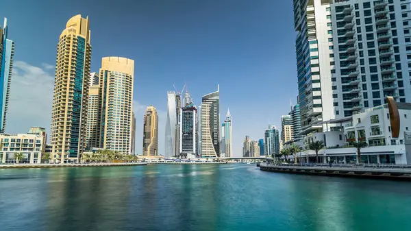 Dubai Marina canal with yachts and modern towers reflected in green water from waterfront in Dubai timelapse hyperlapse, United Arab Emirates. District with artificial canal