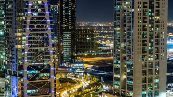 Buildings of Jumeirah Lakes Towers with traffic on the road night aerial timelapse. The JLT district top view from dubai marina skyscraper