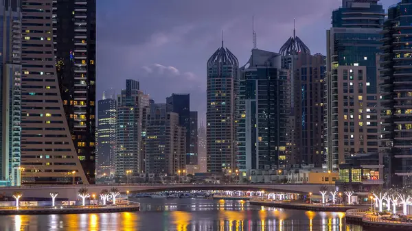 Dubai Marina canal, waterfront with modern towers and yachts reflected in water from bridge in Dubai night to day transition timelapse, United Arab Emirates. Skyscrapers around before sunrise