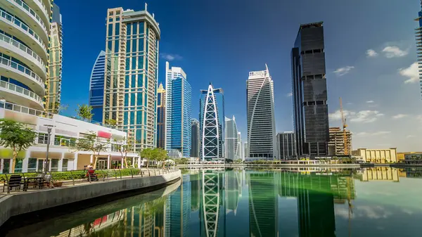 Timelapse hyperlapse view on skyscrapers at waterfront with palms. Residential buildings covered with glass in Jumeirah Lake Towers reflected in water in Dubai, UAE. View from waterfront