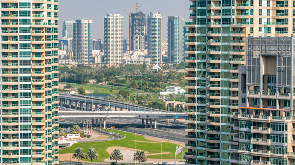 Golf field from top at day time with traffic on sheikh zayed road. Green grass of the golf course against the background the city skyscrapers at sunset. Modern towers of greens district on the side