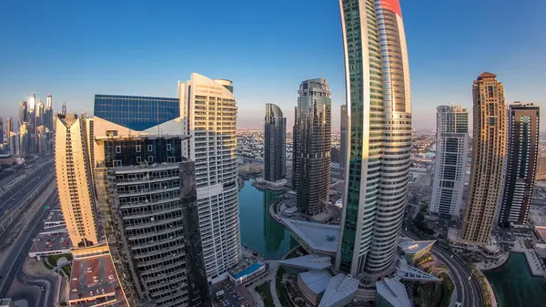 Buildings of Jumeirah Lakes Towers after sunset with traffic on the road day to night transition timelapse. Top view from skyscraper rooftop. Fisheye lens
