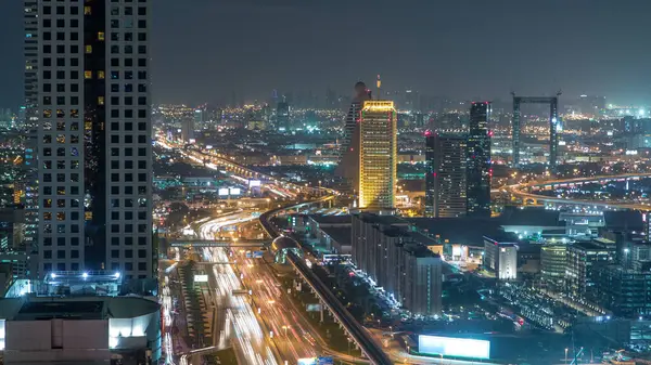 Dubai şehir merkezinde mimarlık gecesi zaman aşımı. Şeyh Zayed yolu üzerindeki aydınlık gökdelenler ve trafik manzaralı hava manzarası. Uzun kuleler ve bulutlu gökyüzü