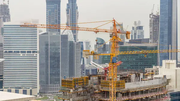 Construction site in Dubai timelapse, United Arab Emirates. Yellow cranes and workers in uniform. Business bay skyscrapers aerial top view